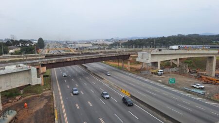 Vista aérea da Rodovia Presidente Dutra em Arujá, mostrando o tráfego de veículos entre viadutos em obras sob céu nublado.